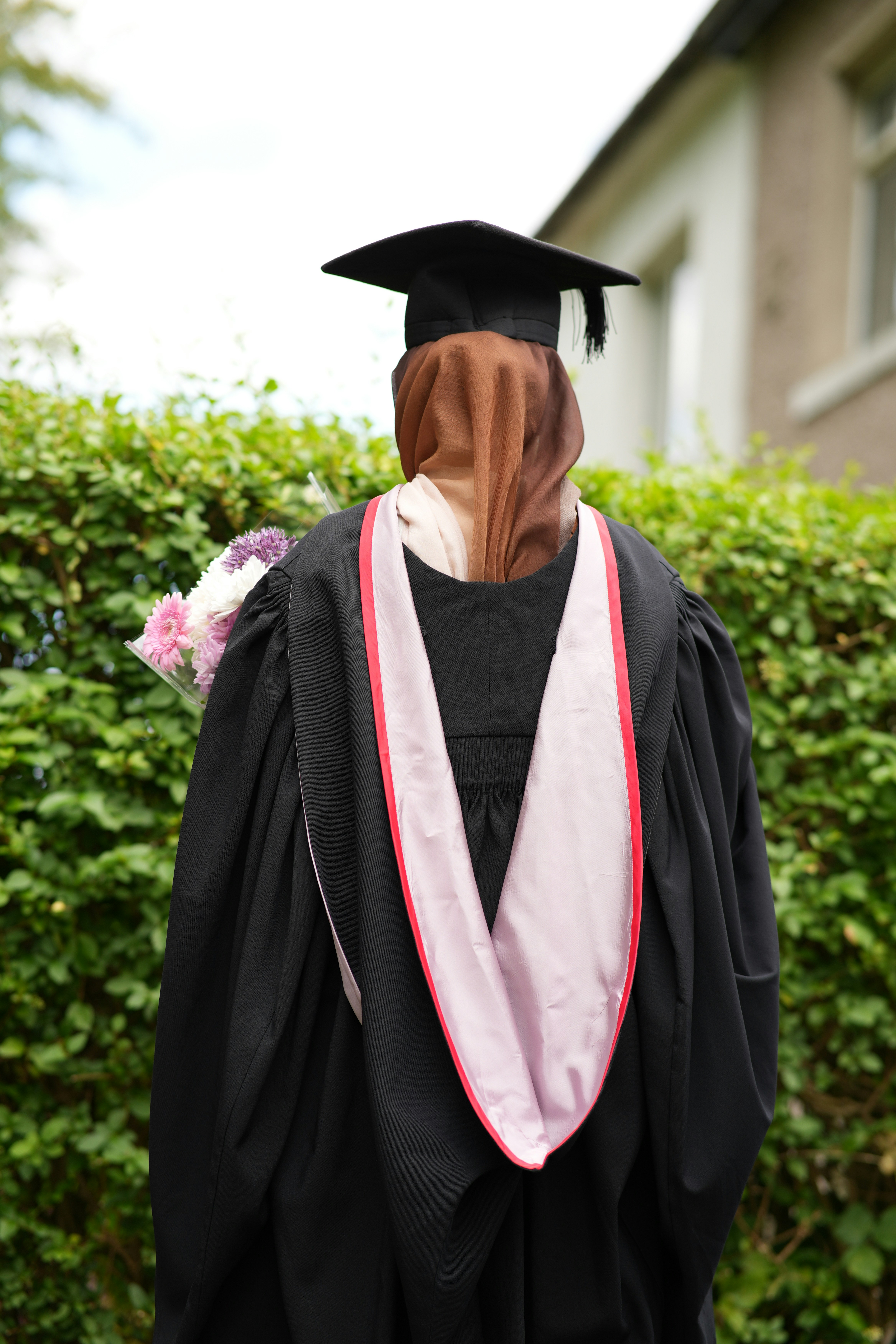 Graduate wearing cap and gown holding bouquet