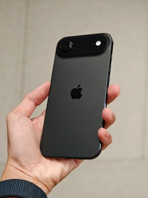 Hand holding a dark gray iPhone with apple logo.