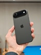 Hand holding a dark grey smartphone with apple logo.