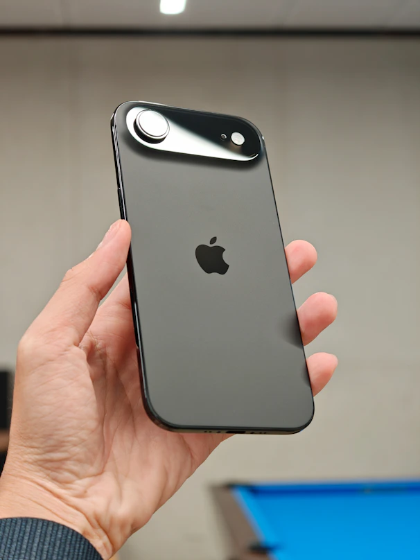 Hand holding a dark gray smartphone with apple logo.