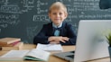 Young boy in a suit at a desk with books.
