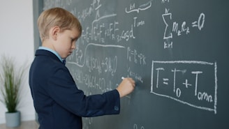 Young boy in suit writing on chalkboard with math equations