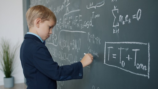 Young boy in suit writing on chalkboard with math equations