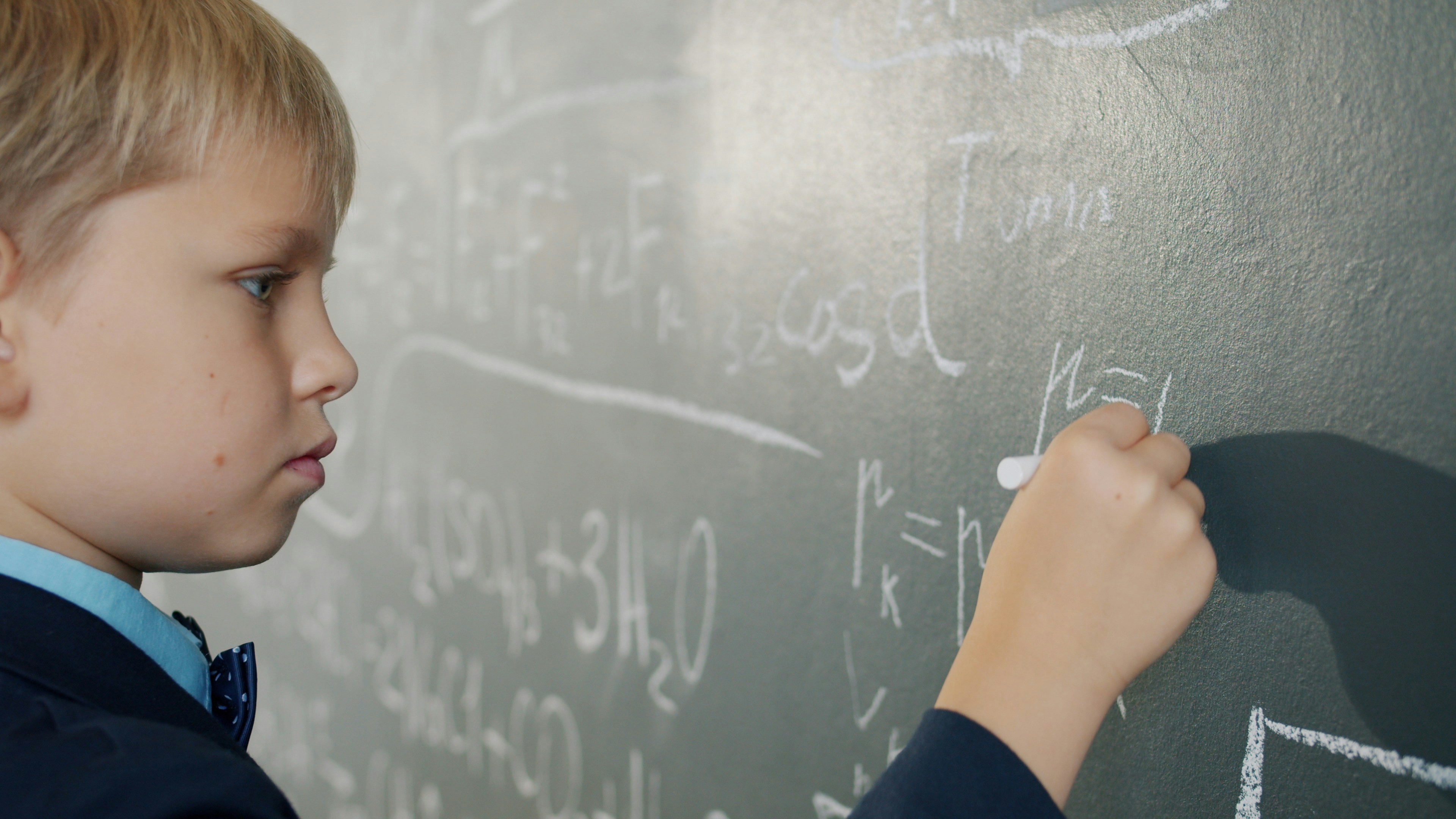 smart schoolboy writing formulas on chalkboard studying alone indoors busy with scientific calculations. People and education concept.