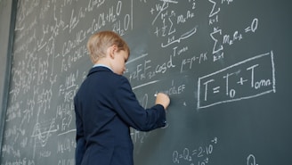Young boy in suit writing equations on chalkboard