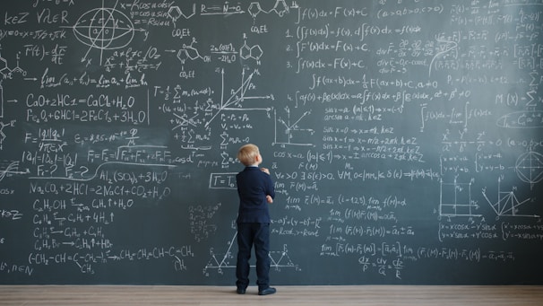 Young boy looking at complex math formulas on blackboard.