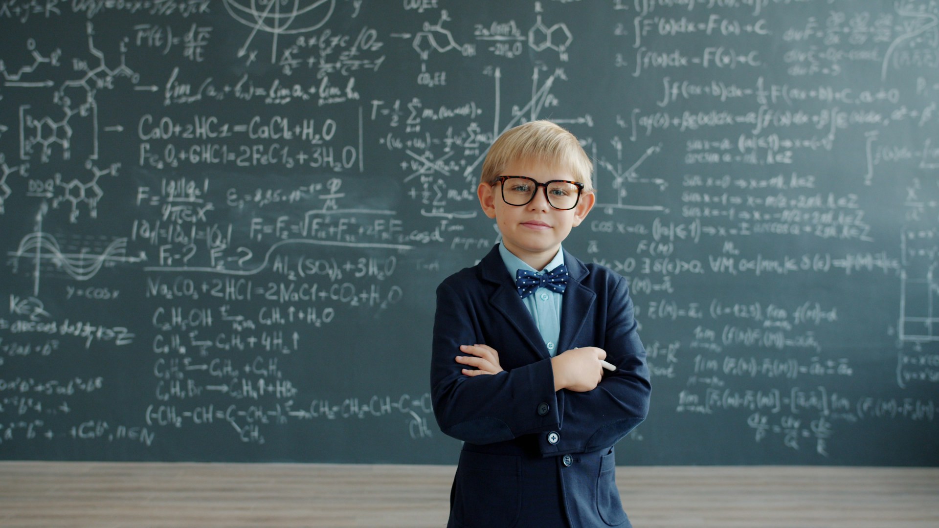 Young boy in suit stands before chalkboard equations