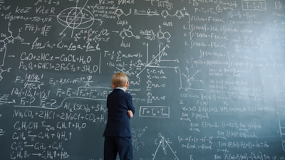 Young boy in suit studies complex math equations on blackboard