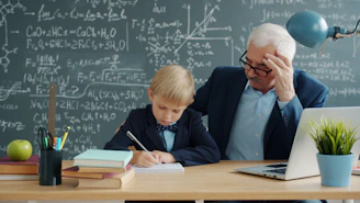 Teacher helping young student with math problems at desk.