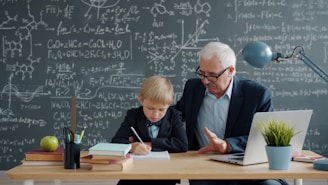 Elderly man teaching young boy math at desk.