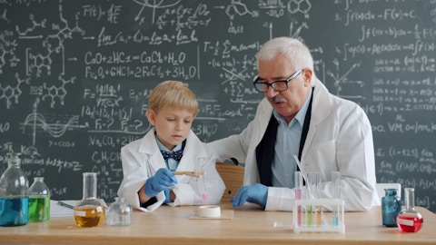 Elderly scientist teaches young boy in lab coat.