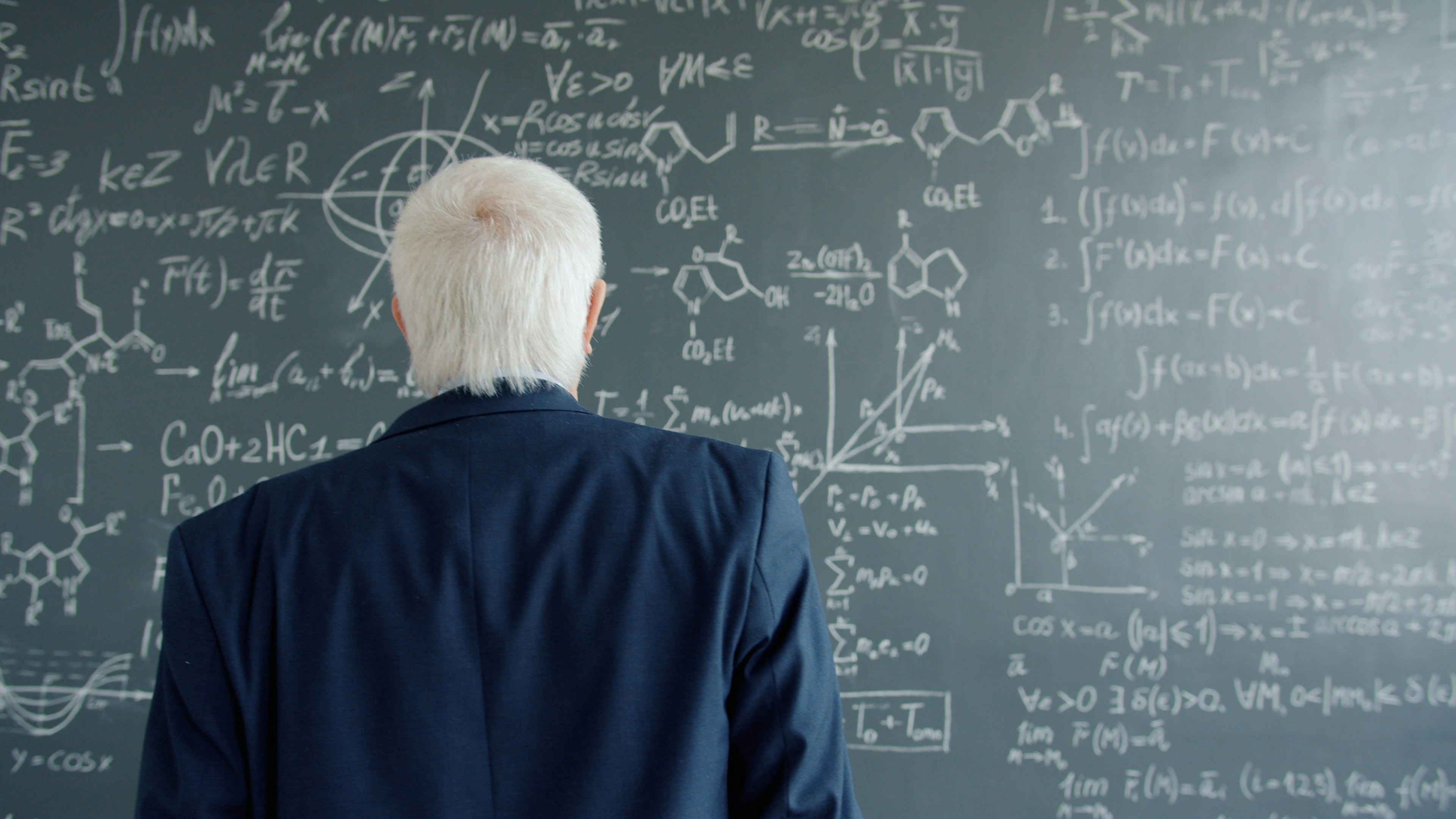 Professor looking at complex mathematical equations on chalkboard