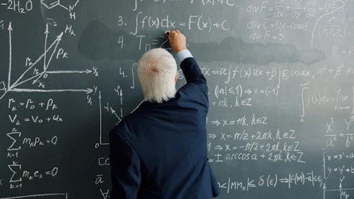 Professor writing mathematical formulas on a blackboard.