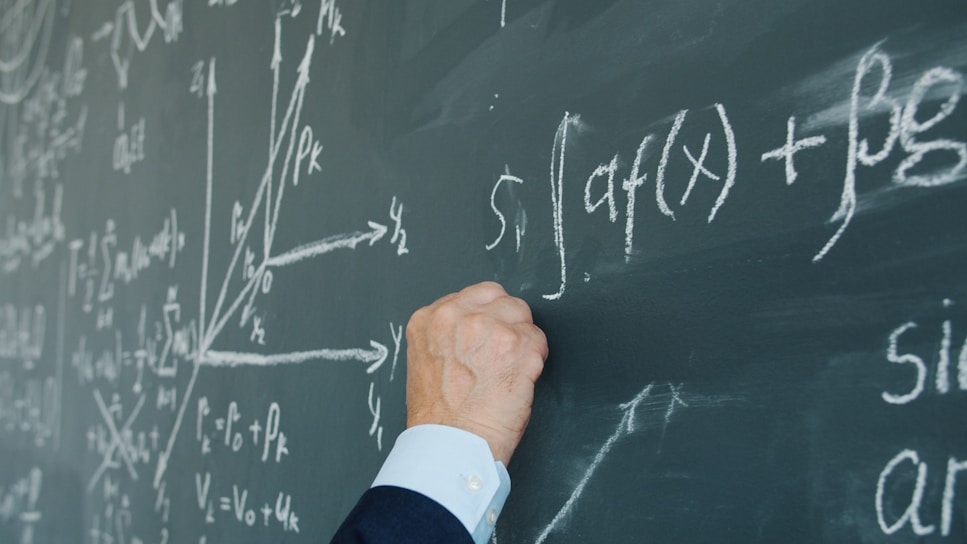 Hand writing mathematical formulas on a chalkboard.
