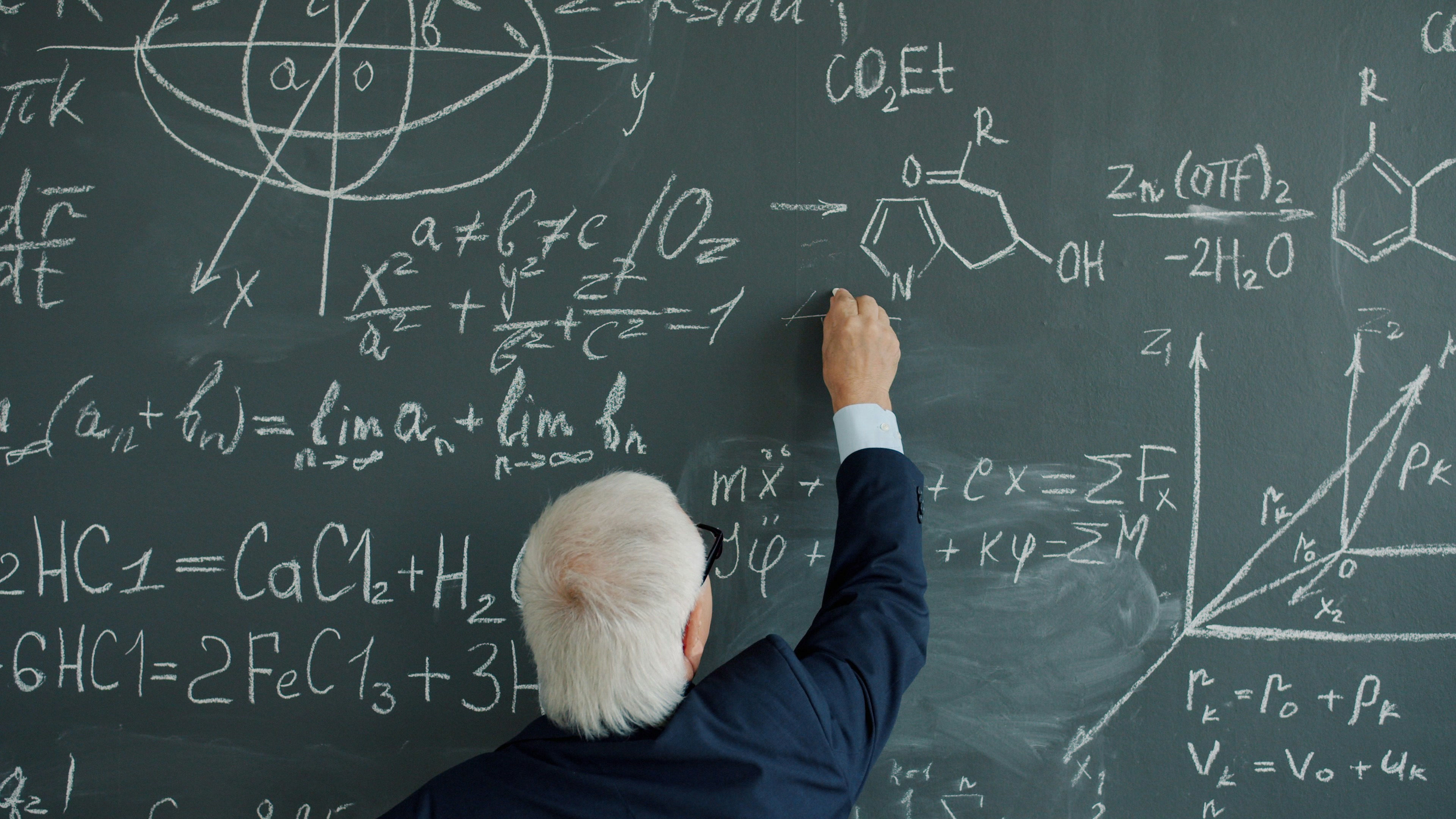 gray-haired man writing formulas on chalk board in college busy with science and calculations. Modern people, education and knowledge concept.