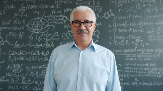Smiling older man in front of chalkboard with formulas.