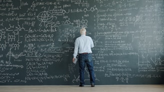 Man writing complex formulas on a chalkboard wall.