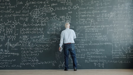 Man writing complex formulas on a chalkboard wall.