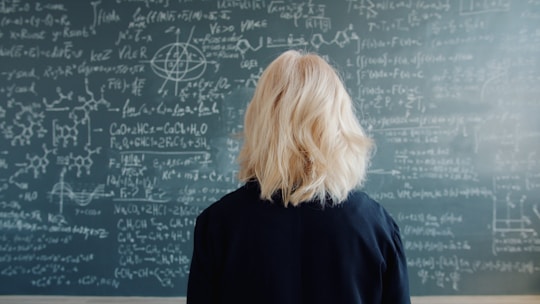 Woman with blonde hair facing a chalkboard with equations.