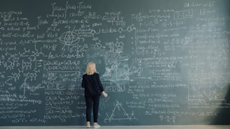 Woman writing complex formulas on a chalkboard wall.