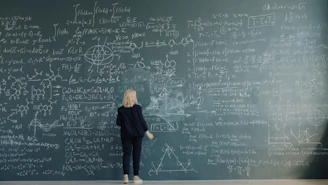 Woman writing complex formulas on a chalkboard wall.