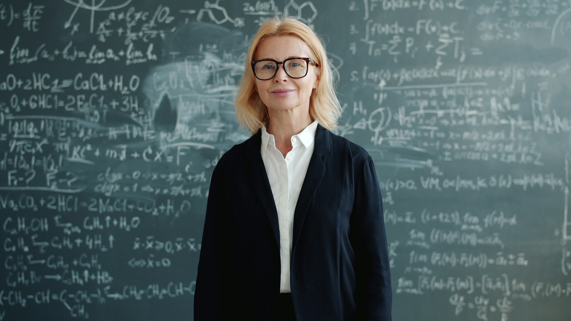 A woman stands in front of a chalkboard with equations.
