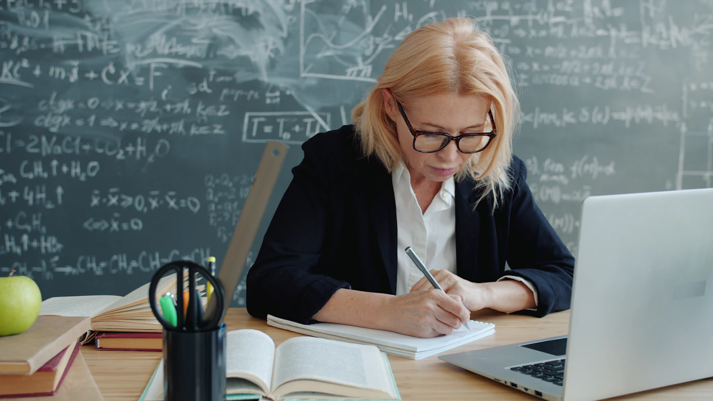 Experienced teacher reviewing lesson notes and laptop at a classroom desk