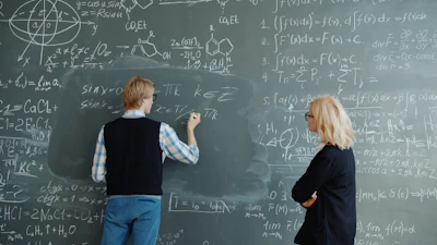 Student writes math equations on blackboard while teacher watches.