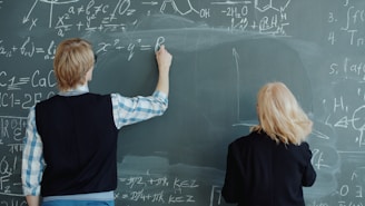 Two people writing math formulas on a chalkboard.