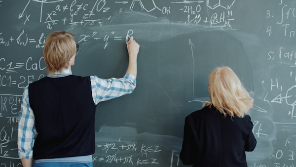 Two people writing math formulas on a chalkboard.