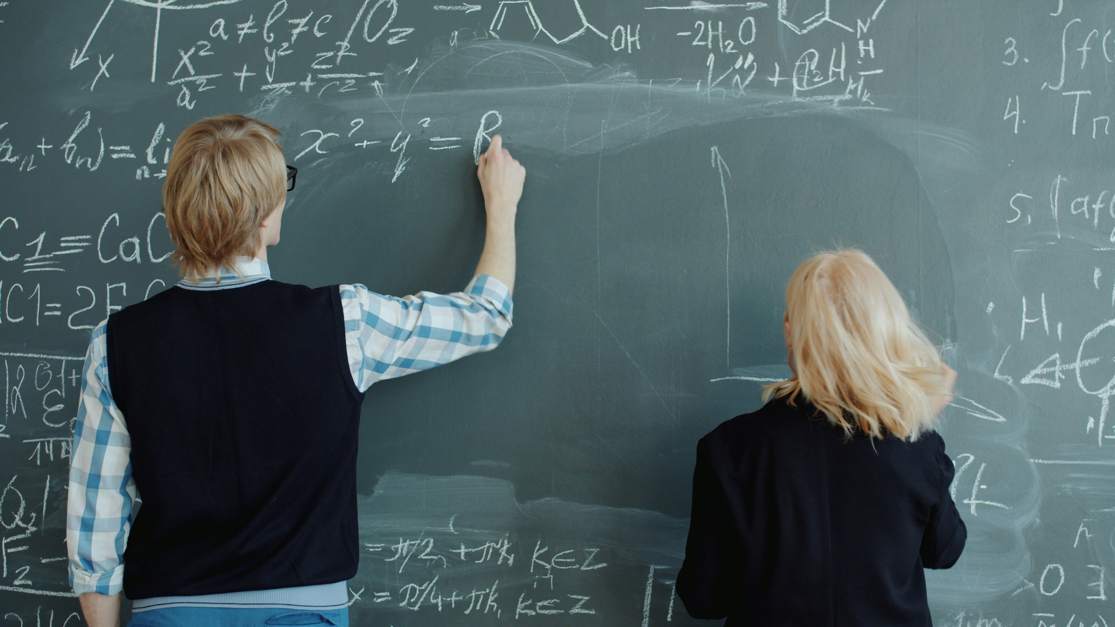 Scientists colleagues man and woman are writing formulas on chalkboard in class drawing busy with theory. Education, people and university concept.