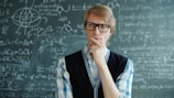 Man with glasses thinking in front of chalkboard