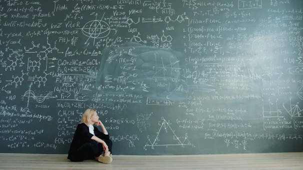 Woman contemplating complex formulas on a blackboard.