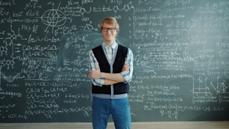 Man in glasses stands before a chalkboard with equations.