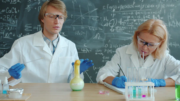 Scientists in lab coats conduct experiment with colorful liquids.