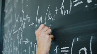 Hand writing mathematical formulas on a blackboard with chalk.