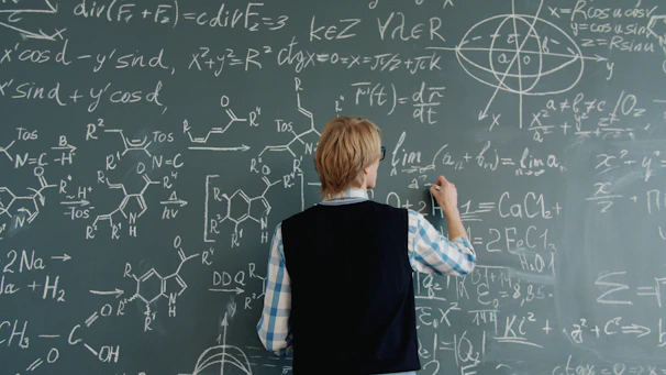 Teacher writing math equations on a chalkboard.