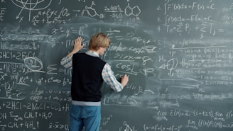 Student writing mathematical formulas on a blackboard.