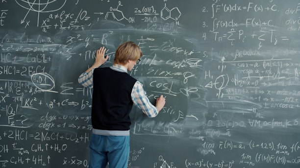 Student writing mathematical formulas on a blackboard.