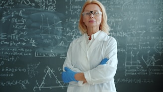 Scientist in lab coat stands before chalkboard with formulas.