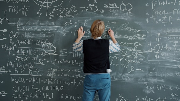 Student writing complex math equations on chalkboard