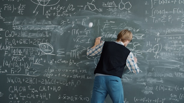 Student writing complex equations on a chalkboard.