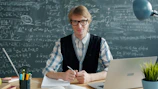 Young man with glasses at a desk with laptop.