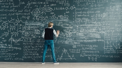 A person writing complex formulas on a chalkboard.