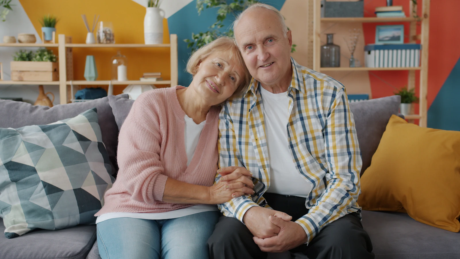 Two older adults holding hands while seated together at home