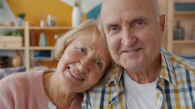 An older couple laughing together indoors, both retired and visibly at ease