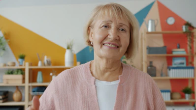 Smiling elderly woman in a pink cardigan indoors.