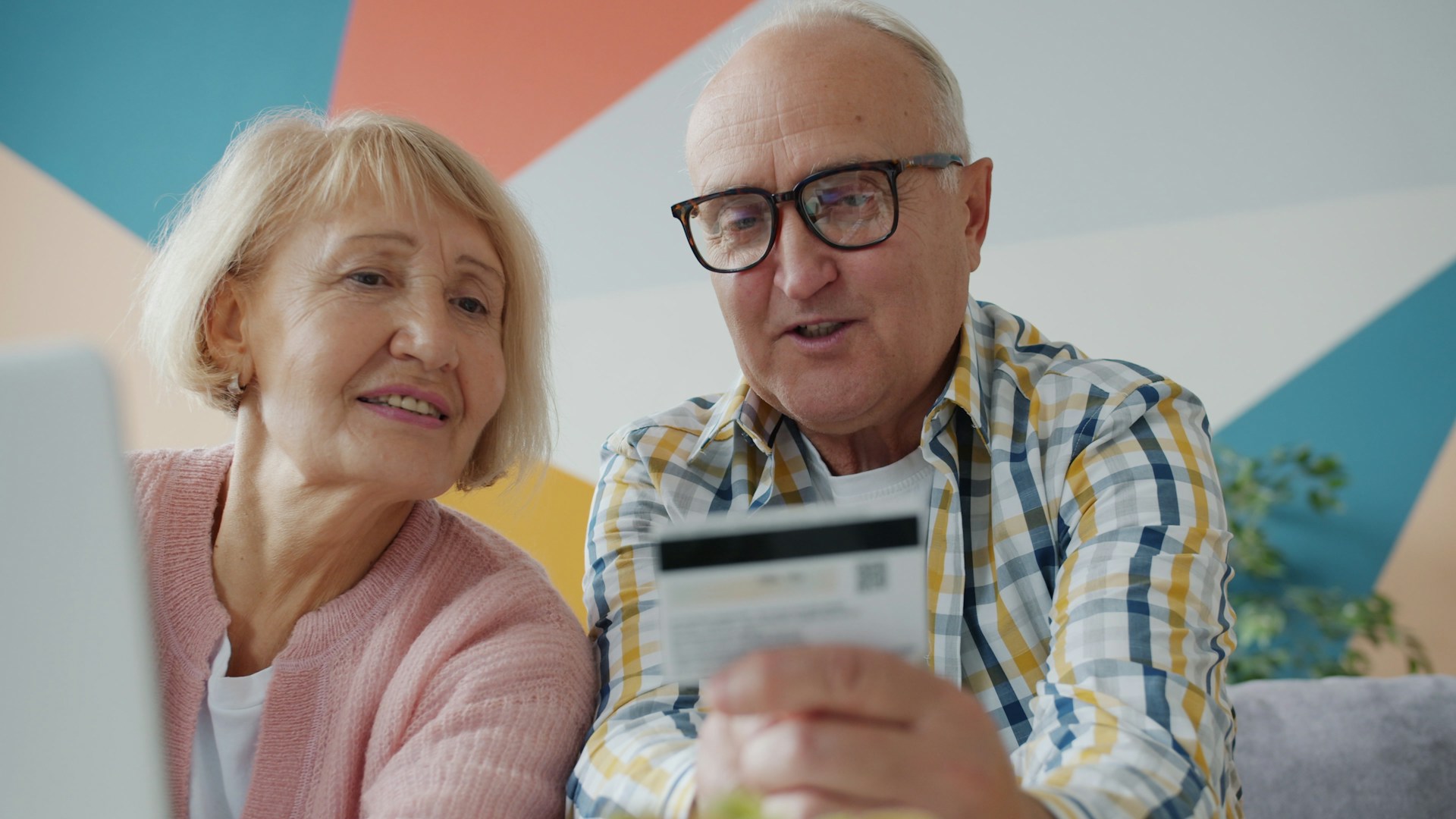 Elderly couple looking at credit card and laptop.