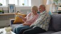Elderly couple watching television on sofa with popcorn.