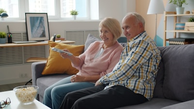 Elderly couple watching television on sofa with popcorn.